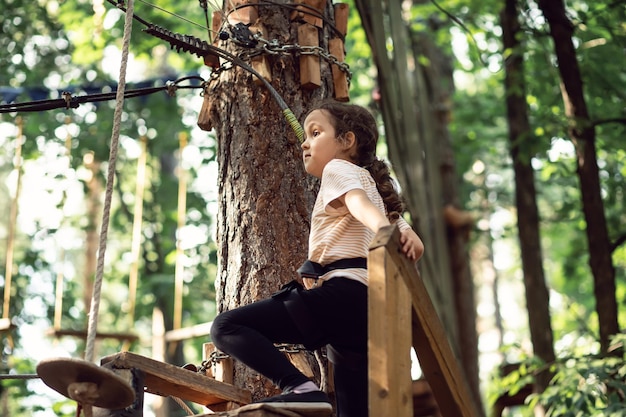 Kleines süßes Mädchen, das Spaß im Abenteuerpark hat. Kinder klettern in einem Seilpark. Sommeraktivitäten für Kinder. Glückliche Kindheit