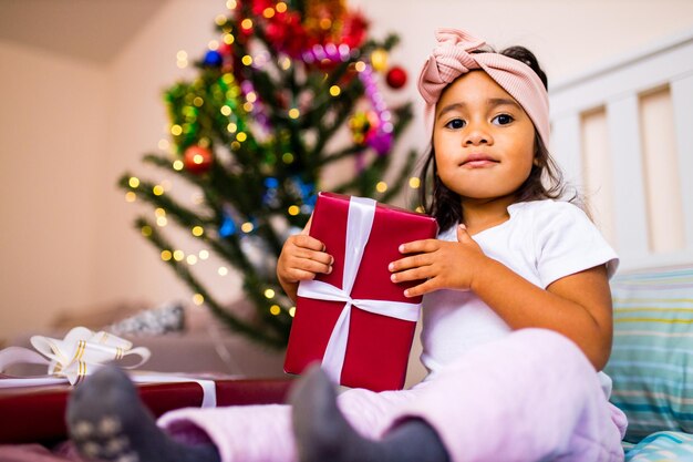 Kleines süßes Mädchen der gemischten Rasse, das am Weihnachtsmorgen im Schlafzimmer aufwacht und einen Wunsch wünscht