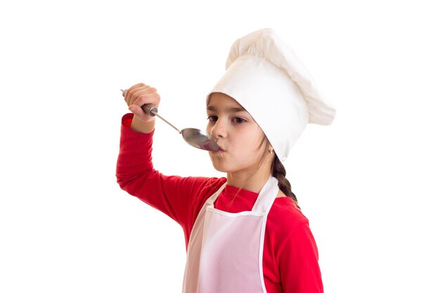 Kleines süßes Mädchen im roten Hemd mit weißer Schürze und Hut mit Schaufel auf weißem Hintergrund im Studio