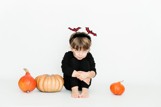 Kleines süßes Mädchen in schwarzer Kleidung unter Kürbissen Halloween-Feier