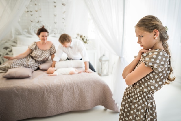 Kleines süßes Mädchen ist eifersüchtig auf ihren neugeborenen Bruder, der auf dem Bett liegt