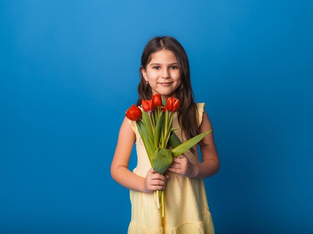 Kleines süßes Mädchen mit einem Strauß Tulpen auf blauem Hintergrund Fröhlicher Frauentag Platz für Text Lebhafte Emotionen 8. März