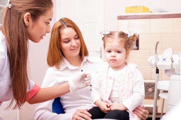 Kleines süßes Mädchen mit Mutter besucht eine Zahnärztin