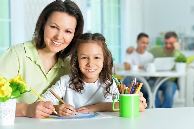 Kleines süßes Mädchen mit Mutter, die zu Hause am Tisch zeichnet