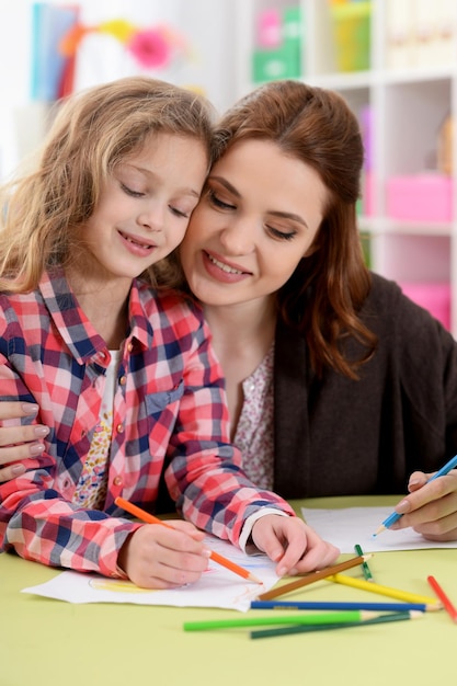 Kleines süßes Mädchen mit Mutter, die zu Hause am Tisch zeichnet