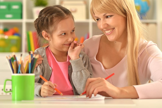 Kleines süßes Mädchen mit Mutter, die zu Hause zeichnet