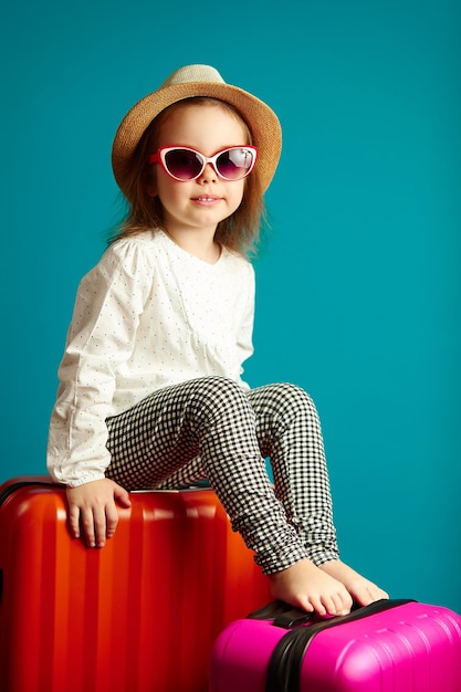 Kleines süßes Mädchen mit Strohhut und Sonnenbrille, das auf Koffern sitzt