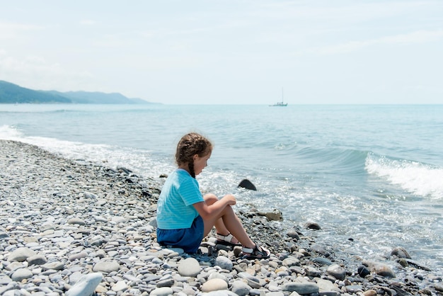 Kleines süßes Mädchen sitzt an einem Kiesstrand und spielt mit Kieselsteinen