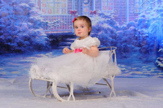Kleines süßes Mädchen sitzt in einem Schlitten auf dem Schnee.