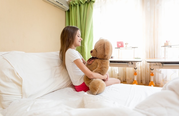 Kleines süßes Mädchen sitzt umarmt ihren Teddybären