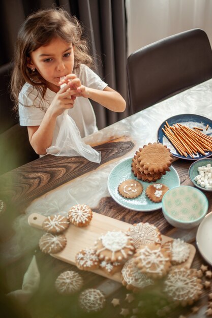 Kleines süßes Mädchen verziert Lebkuchen mit Zuckerglasur. Vorbereitung für das Weihnachtskonzept.