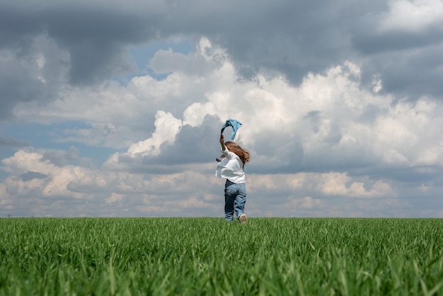 Kleines Teenager-Mädchen, das auf einem Feld mit grünem Gras vor dem Hintergrund eines bewölkten Himmels läuft