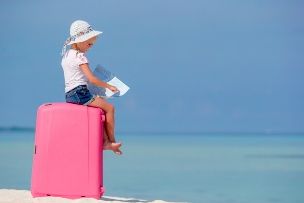 Kleines Touristenmädchen mit großem Koffer auf tropischem weißem Strand