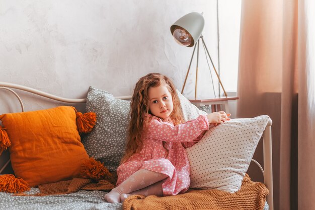 Kleines Vintage-Mädchen sitzt auf einem Bett in einem Kinderzimmer und träumt