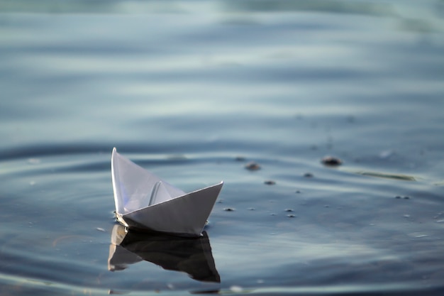 Kleines weißes Origami-Papierboot, das im blauen Fluss schwimmt