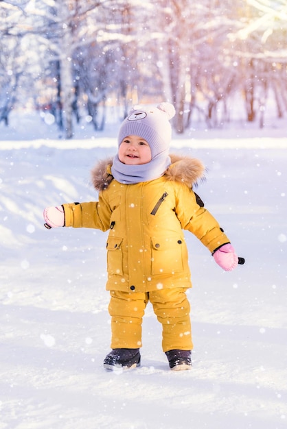 Kleinkind 12-17 Monate alt in gelber Winterkleidung freut sich über den gefallenen Schnee beim Spaziergang im Winterpark