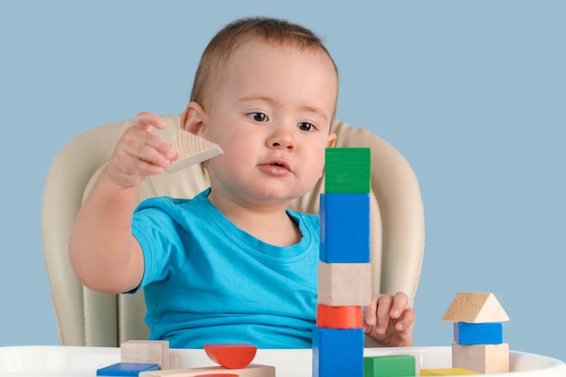 Kleinkind 1217 Monate Bau eines Turms aus farbigen Holzwürfeln auf einem Kinderstuhl auf blauem Hintergrund