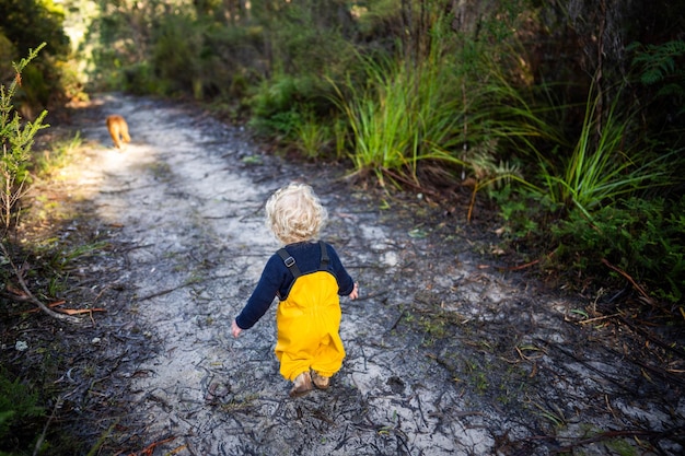Kleinkind erkundet im Winter in gelben Overalls den Wald