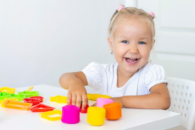 Kleinkind formt aus farbigem Plastilin auf einem weißen Tisch