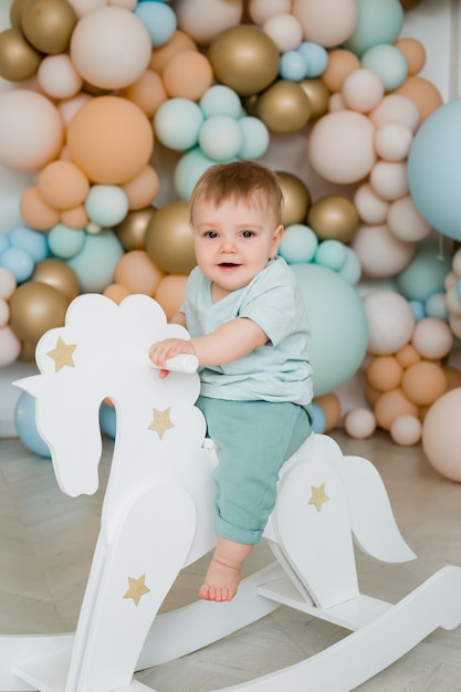 Kleinkind Kind Baby Kind Kleinkind sitzend reiten weißes kleines hölzernes Pferdespielzeug. Fotozone von Luftballons.