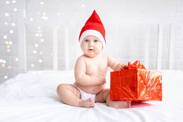 Kleinkind Kind in roter Weihnachtsmütze sitzt mit einem Geschenk auf einem weißen Hintergrund Neujahr Weihnachtsferien