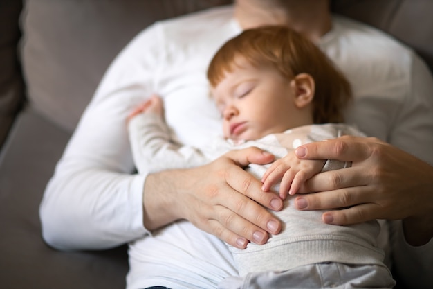 Kleinkind und Papa schlafen tagsüber auf der Couch Konzept Kindertag und elterliche Betreuung konzentrieren sich auf die Hände