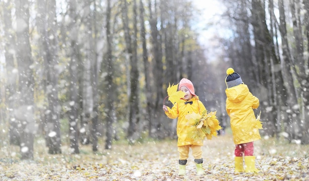 Kleinkinder bei einem Spaziergang im Herbstpark. Erster Frost und der erste Schnee im Herbstwald. Kinder spielen im Park mit Schnee und Blättern.