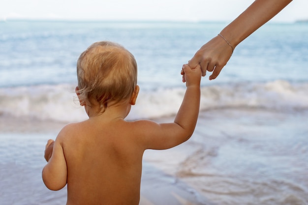 Kleinkindhändchenhalten mit gesichtsloser Mutter im Strand