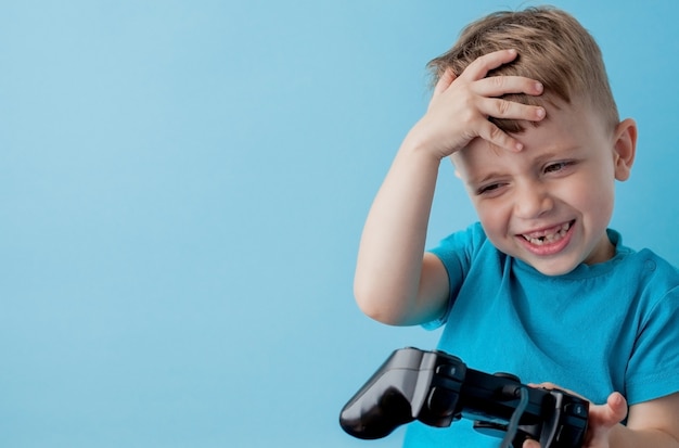 Kleinkindjunge 2-3 jahre alte tragende blaue kleidung halten in der hand steuerknüppel für gameson blaues hintergrundkinderstudioporträt. leutekindheits-lebensstilkonzept. mock-up textfreiraum