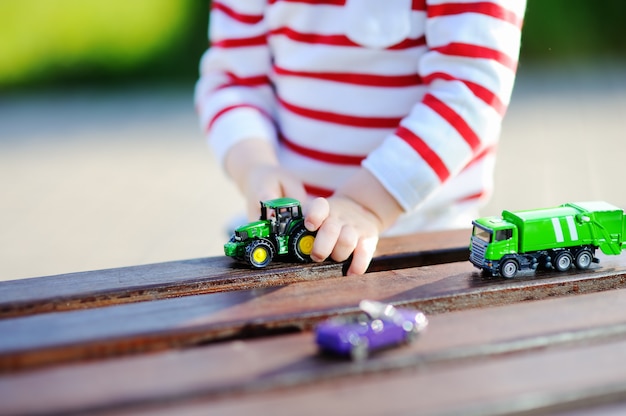 Kleinkindjunge, der draußen mit Spielzeugautos am warmen Sommertag spielt