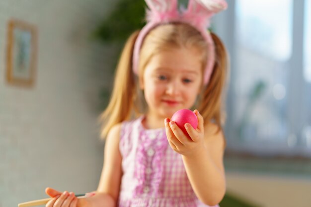 Kleinkindmädchen mit Hasenohren, die Eier für Ostern färben