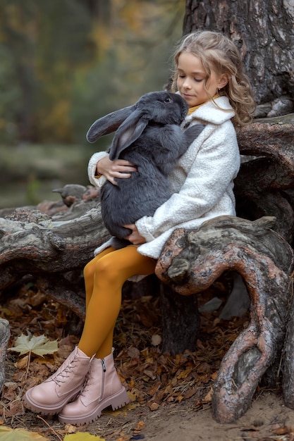 Kleinkindmädchen umarmt ein riesiges graues Kaninchen im Herbstwald Konzept Liebe zur Natur und Liebe zu Tieren