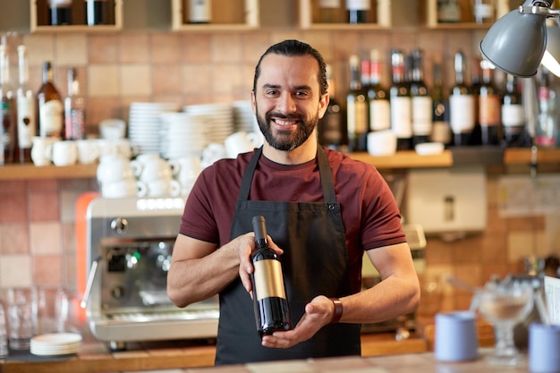 Kleinunternehmen, alkoholische Getränke, Menschen und Service-Konzept - glücklicher Mann oder Kellner mit einer Flasche Rotwein an der Bar