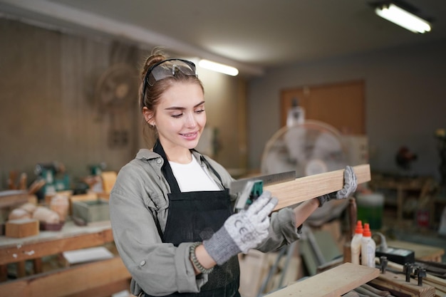 Kleinunternehmen einer jungen Frau Schöne junge Arbeitnehmerin in einem Möbelwerkraum, der Holz misst