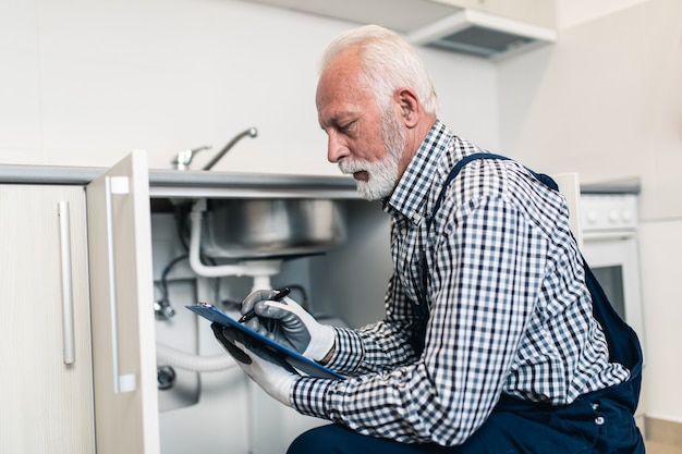 Klempner des älteren Mannes, der mit Klempnerarbeitwerkzeugen auf der Küche arbeitet. Renovierung.