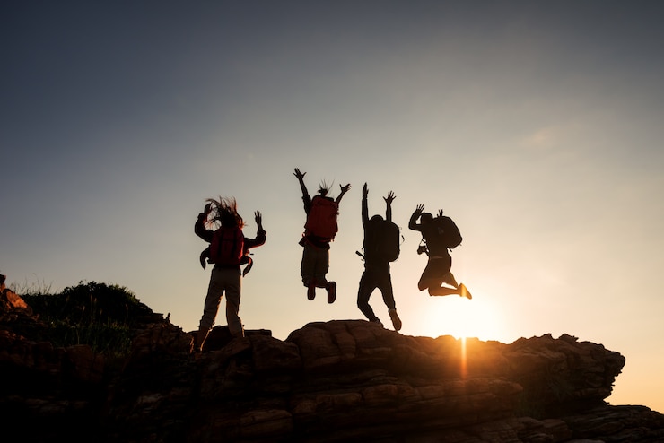 Foto kletternde gruppenfreunde, die auf spitzenberg und erstaunlichen sonnenunterganghimmel springen.