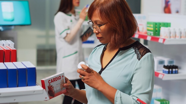 Klientin, die sich kardiologische Pillenboxen ansieht, um eine Behandlung zu kaufen, und ein medizinisches Geschäft besucht. Frau überprüft Verpackungen von pharmazeutischen Produkten und Flaschen mit Medikamenten, um Krankheiten zu heilen. Handschuss.