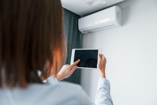 Klimaanlage per Tablet steuern Junge Frau ist tagsüber drinnen im Zimmer eines modernen Hauses