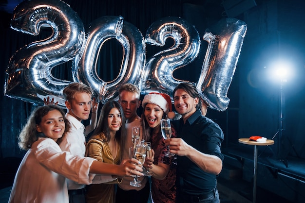 Klopfende Brille. Fröhliche Gruppe von Menschen mit Getränken und Luftballons in den Händen, die das neue 2021-Jahr feiern.