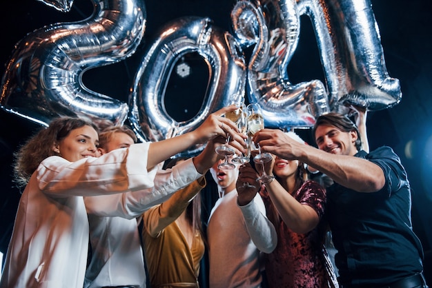 Klopfende Brille. Fröhliche Gruppe von Menschen mit Getränken und Luftballons in den Händen, die das neue 2021-Jahr feiern.