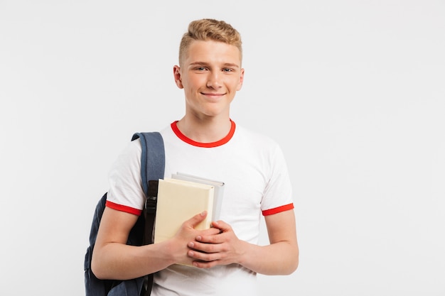 kluger Inhalt Student Kerl, der Rucksack trägt, der lächelt und Sie mit Büchern in den Händen lokalisiert auf Weiß betrachtet