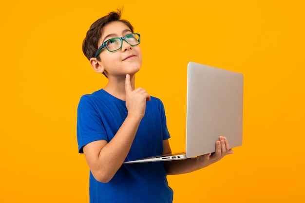 Foto kluger junge in einem blauen t-shirt, der denkt, einen laptop in seinen händen auf gelb zu halten