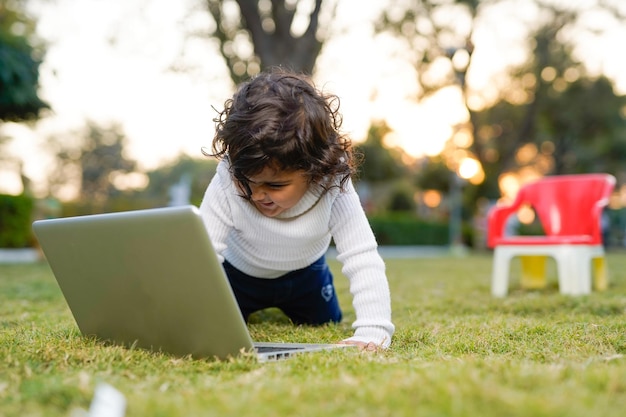 Kluger kleiner Junge, der im Garten spielt, während er Laptop auf dem Wiesenhaus-Versicherungskonzept verwendet