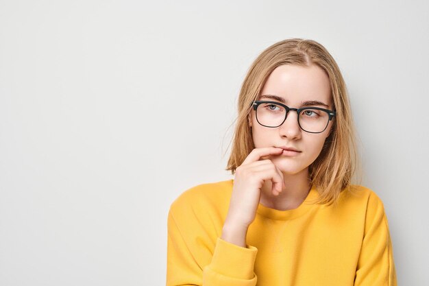 Kluges blondes Studentenmädchen mit Brille berührt Kinn denkt wählt isoliert auf weißem Studio-Hintergrund mit Kopierraum Selbstvertrauen kluges Genie