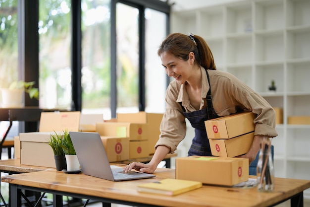 KMU-Unternehmer Kleinunternehmer Online-VerkaufsideenGlückliche junge asiatische Geschäftsinhaber arbeiten am Computer und liefern eine Kiste zu Hause