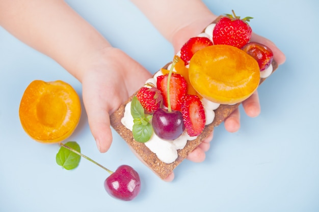 Knäckebrot mit Frischkäse, Obst und Beeren in einer Kinderhand