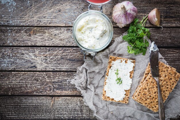 Knäckebrottoast mit hausgemachtem Kräuter- und Knoblauchhüttenkäse auf Holzhintergrund, Ansicht von oben