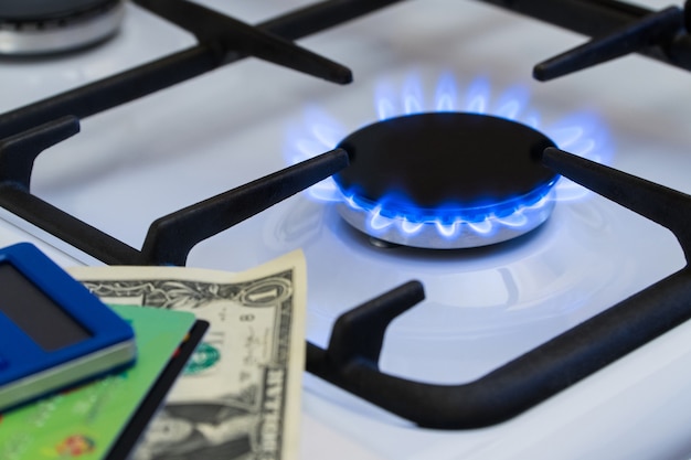 Knappheit und Gaskrise. Geld und ein Taschenrechner auf dem Hintergrund eines brennenden Gasherdes