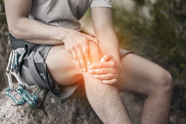 Knieverletzung und Schmerzen bei einem Mann, der auf einem Felsen sitzt, um eine Pause beim Wandern oder Bergsteigen in der Natur zu machen CGI von Beschwerden durch Krämpfe während des Trainings oder Sporttrainings in einem Wald