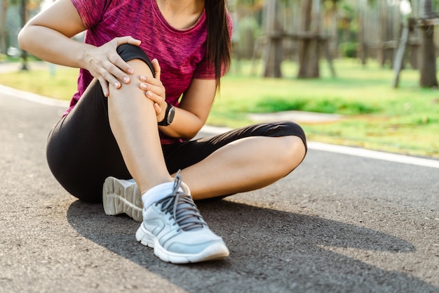 Knieverletzungen. Sportfrau mit starken athletischen Beinen, die Knie mit ihren Händen im Schmerz halten, nachdem sie Muskelverletzung während eines Lauftrainingstrainings auf der Laufbahn erlitten haben. Gesundheits- und Sportkonzept.